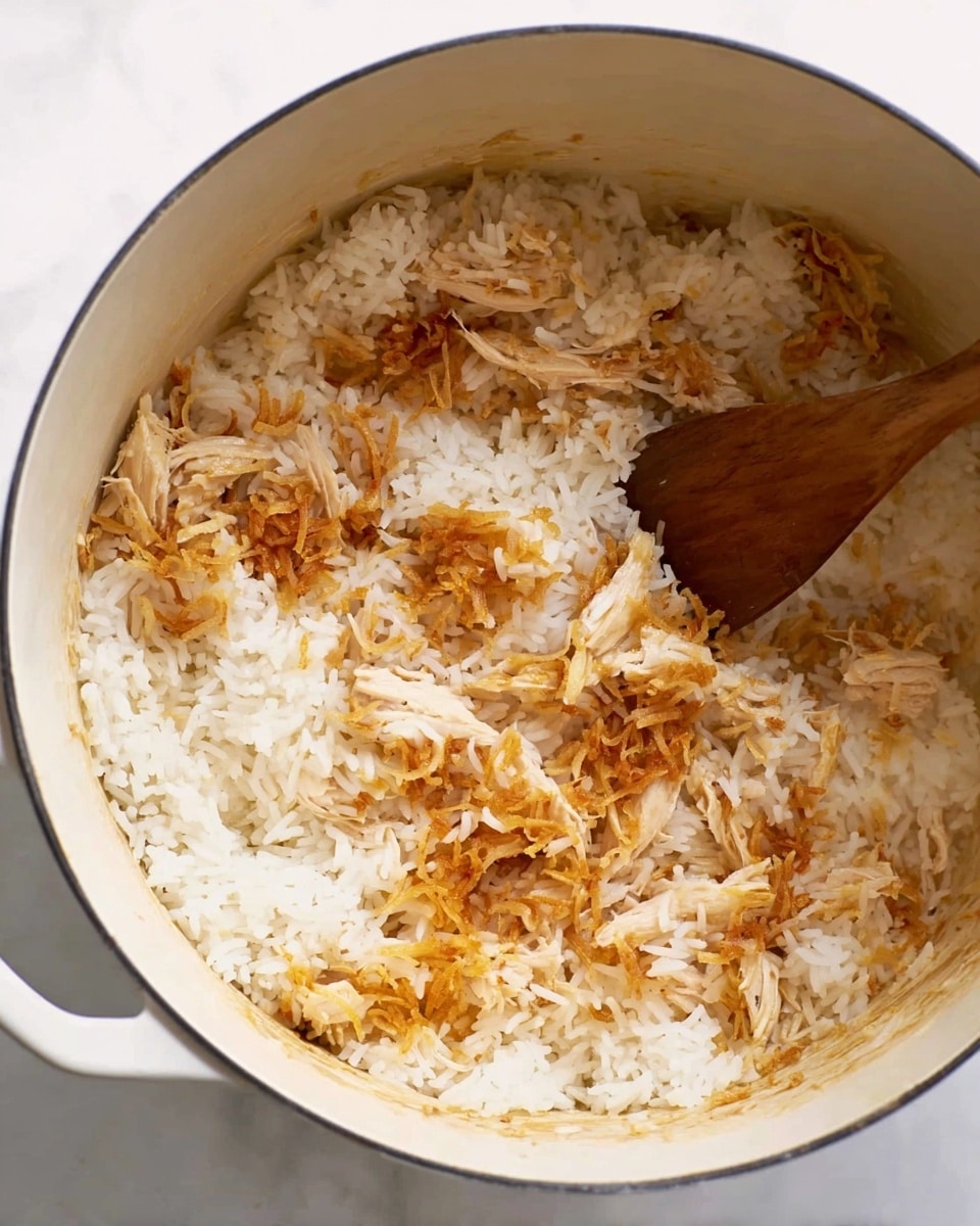 Inside a white pot, there is a mix of white rice and shredded light brown chicken pieces. Some crispy golden brown fried onion bits are sprinkled on top of the rice and chicken. A wooden spoon is partially placed under the rice and chicken mixture, stirring it gently. The inside of the pot shows slight marks from cooking. The pot is placed on a white marbled surface. photo taken with an iphone --ar 4:5 --v 7