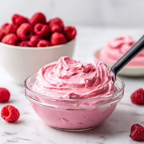 The image shows two clear glass bowls placed side by side on a white marbled surface. The bowl on the left contains a bright red, slightly chunky sauce with a rich and thick texture. The bowl on the right holds a creamy, pale yellow mixture with a smooth and soft texture, showing swirls from mixing. Both bowls are filled only partway, and the focus is on the vibrant color and texture contrast between the two mixtures. Photo taken with an iphone --ar 4:5 --v 7