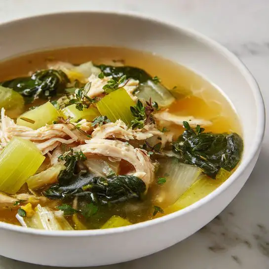 The image shows a close-up of a white bowl filled with a clear chicken soup. The soup has five visible layers: the bottom layer is a light yellowish broth, the second layer has translucent pieces of cooked onions, the third layer consists of light green celery pieces, the fourth layer features bright dark green spinach leaves and some yellowish-green cooked greens, and the top layer shows chunks of tender white shredded chicken mixed throughout. Small bits of green herbs are scattered on top. The bowl rests on a white marbled surface. Photo taken with an iphone --ar 4:5 --v 7