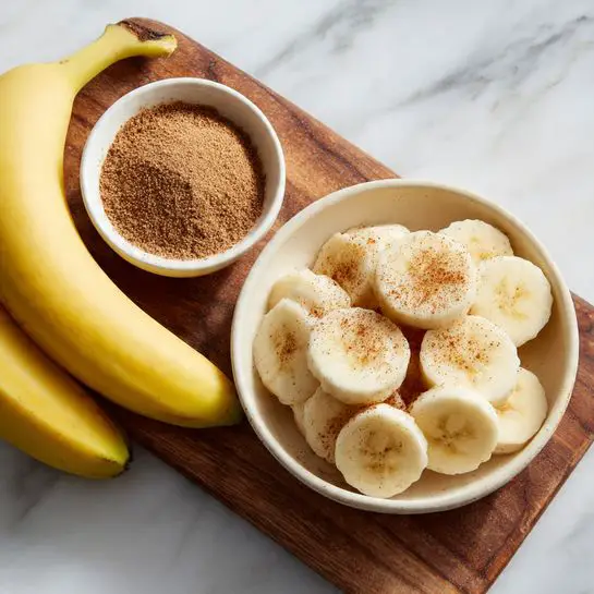 The image shows two ripe yellow bananas lying side by side on a white marbled surface next to a small white bowl filled with a mix of light and darker brown powders, likely sugar and cinnamon. Beside this, there is a wooden board topped with several neatly arranged banana slices, which are creamy white with light brown centers. The setup is clean and simple, highlighting the fresh bananas and spice mix clearly. photo taken with an iphone --ar 4:5 --v 7