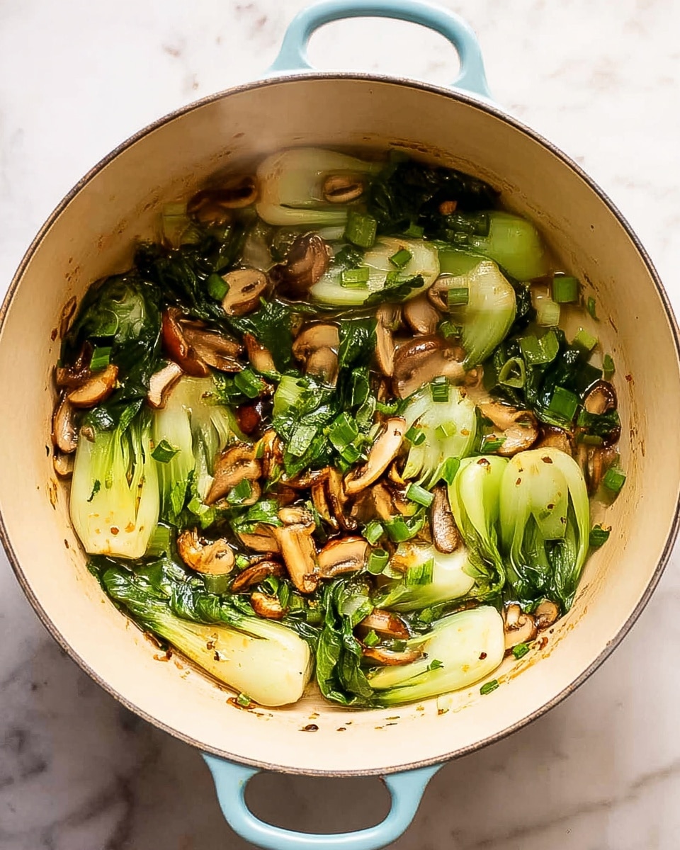 A light blue pot filled with cooked vegetables, mostly green bok choy with leafy tops and light stalks, mixed with browned sliced mushrooms, and small bits of chopped green herbs, all sitting on the creamy beige inner surface of the pot. The pot rests on a white marbled surface with steam rising slightly from the warm vegetables inside. The mix is scattered evenly across the center of the pot, showing a fresh, soft texture in a natural cooking state, photo taken with an iphone --ar 4:5 --v 7