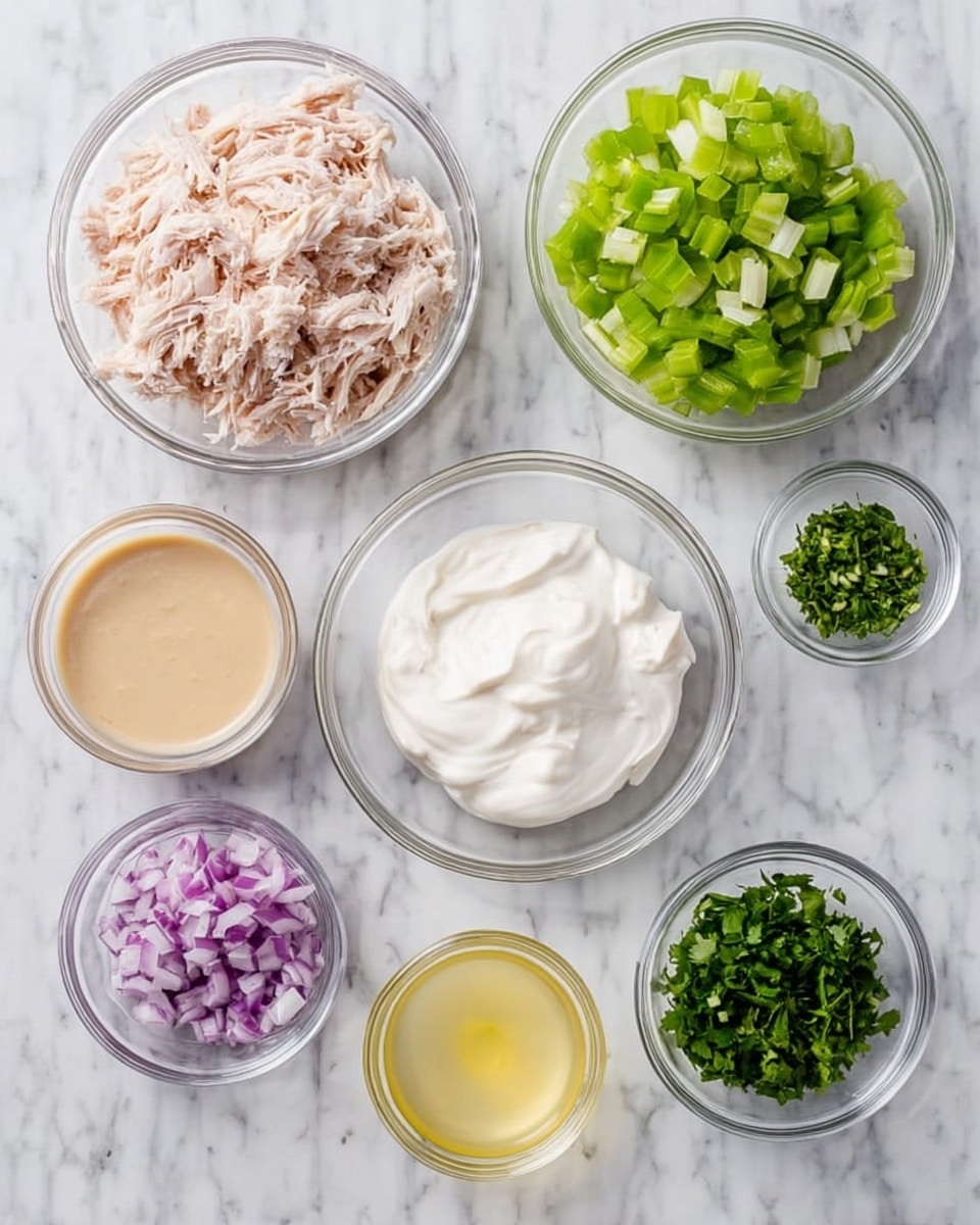 The image shows seven clear glass bowls arranged on a white marbled surface, each containing different ingredients for a dish. Starting from the top left, there is a bowl filled with shredded pale pink chicken. Next to it on the right is a bowl filled with chopped bright green celery. On the top right, a bowl holds a smooth white creamy substance. Below these, in the lower left area, a small bowl contains a creamy light brown sauce. To its right, a bowl filled with pale yellow lemon juice is placed. Next, there is a small bowl containing finely diced purple onion. On the bottom right, a small bowl holds bright green chopped herbs. The setup is neat and simple, with each ingredient clearly visible. photo taken with an iphone --ar 4:5 --v 7