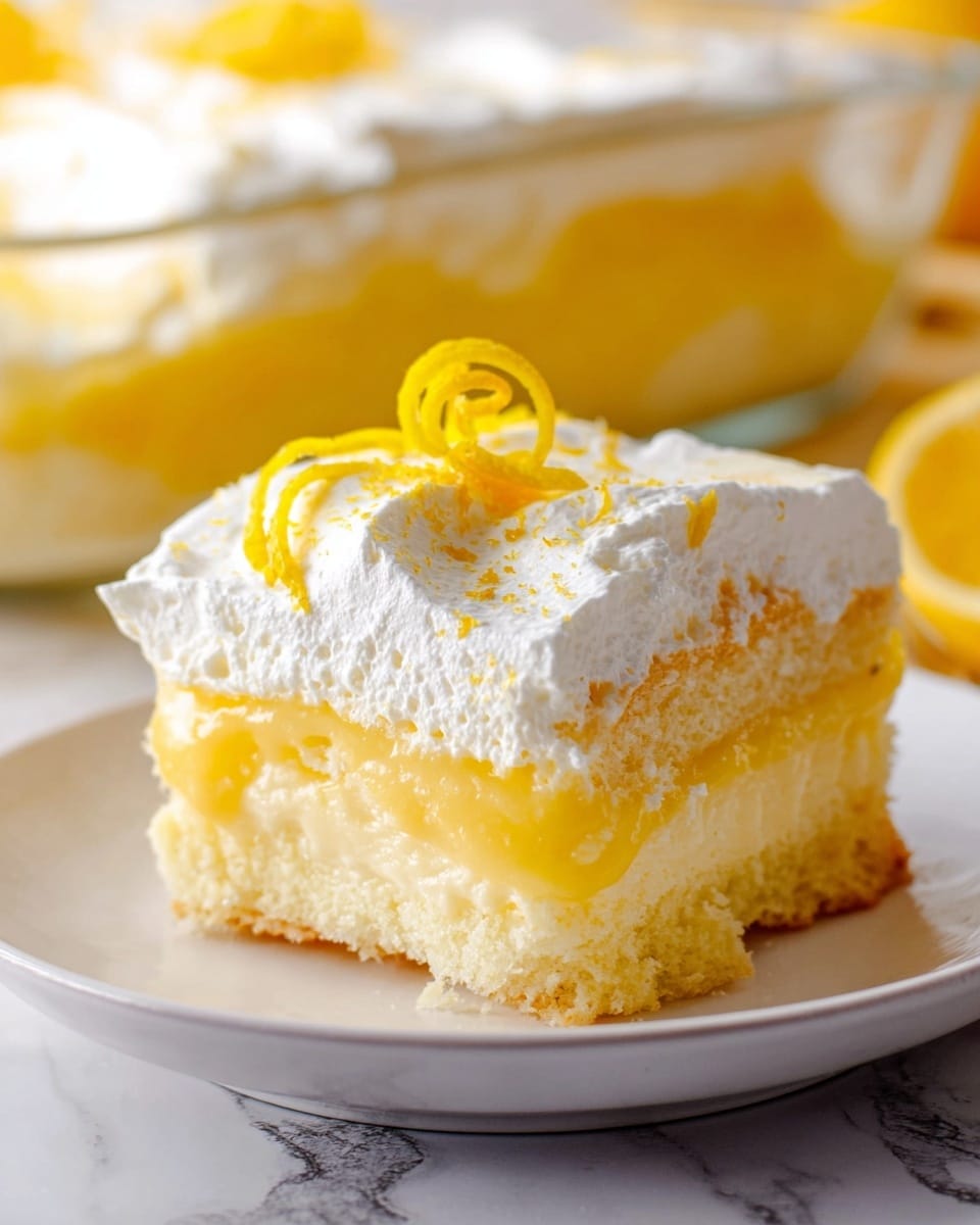 The image shows a creamy lemon dessert with three visible layers on a white plate placed on a white marbled surface. The bottom layer is a light yellow sponge cake with a soft texture. Above it is a thick, smooth yellow lemon filling that looks rich and glossy. The top layer is a thick, white whipped cream that covers the lemon filling evenly, with a curly lemon peel garnish on top for decoration. In the background, a glass dish with more of the dessert can be seen, partially blurred but showing the same layers and textures. photo taken with an iphone --ar 4:5 --v 7