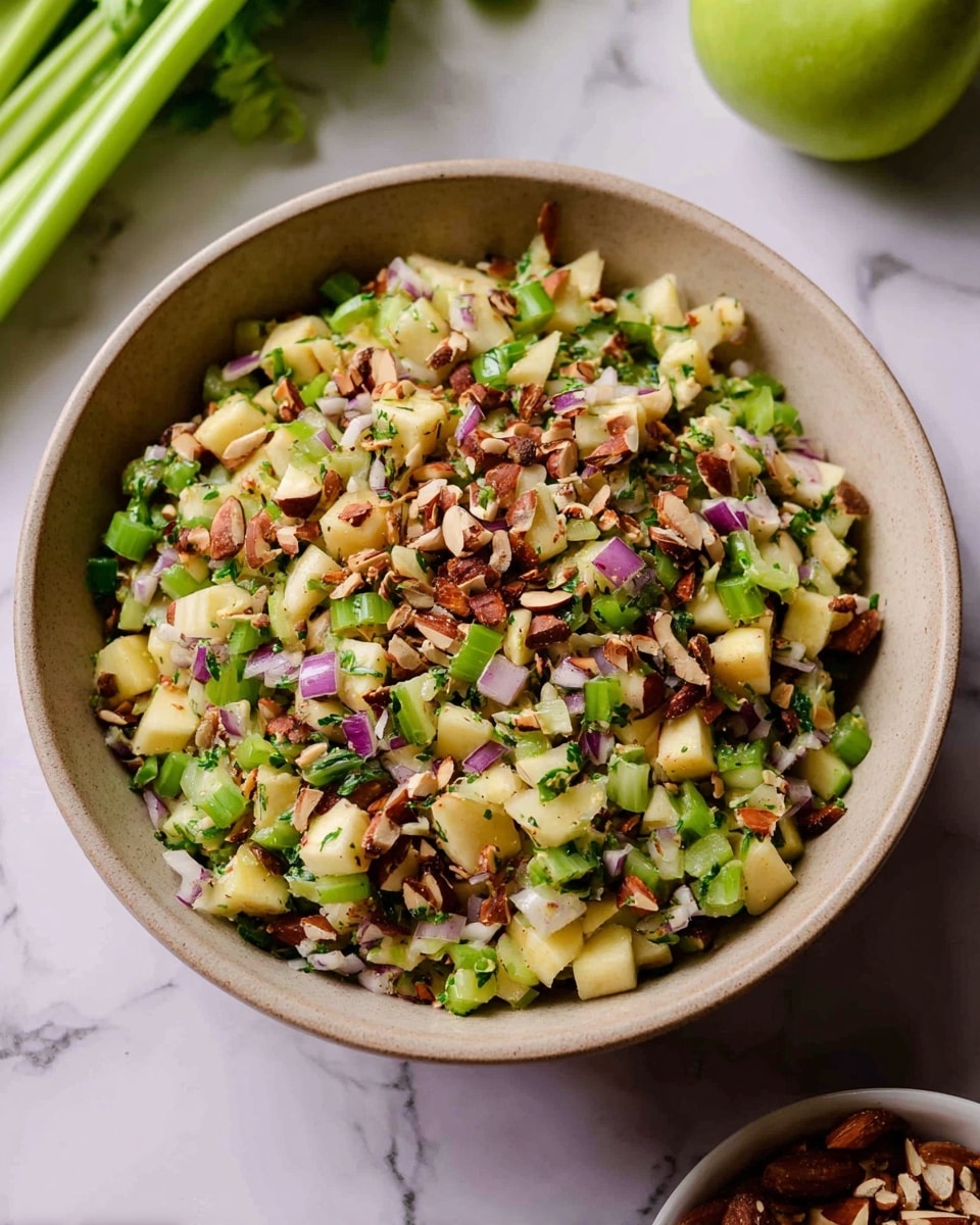 A light brown bowl filled with a colorful salad made of three main layers: a base layer of small green celery pieces and bits of pale yellow apple chunks mixed evenly, a middle layer of finely chopped light purple onion pieces scattered throughout, and topped with a layer of chopped brown almonds giving a crunchy texture. The salad has a fresh, bright look with green herbs mixed inside. The bowl sits on a white marbled surface with some celery stalks and a green apple near it in soft focus. Photo taken with an iphone --ar 4:5 --v 7