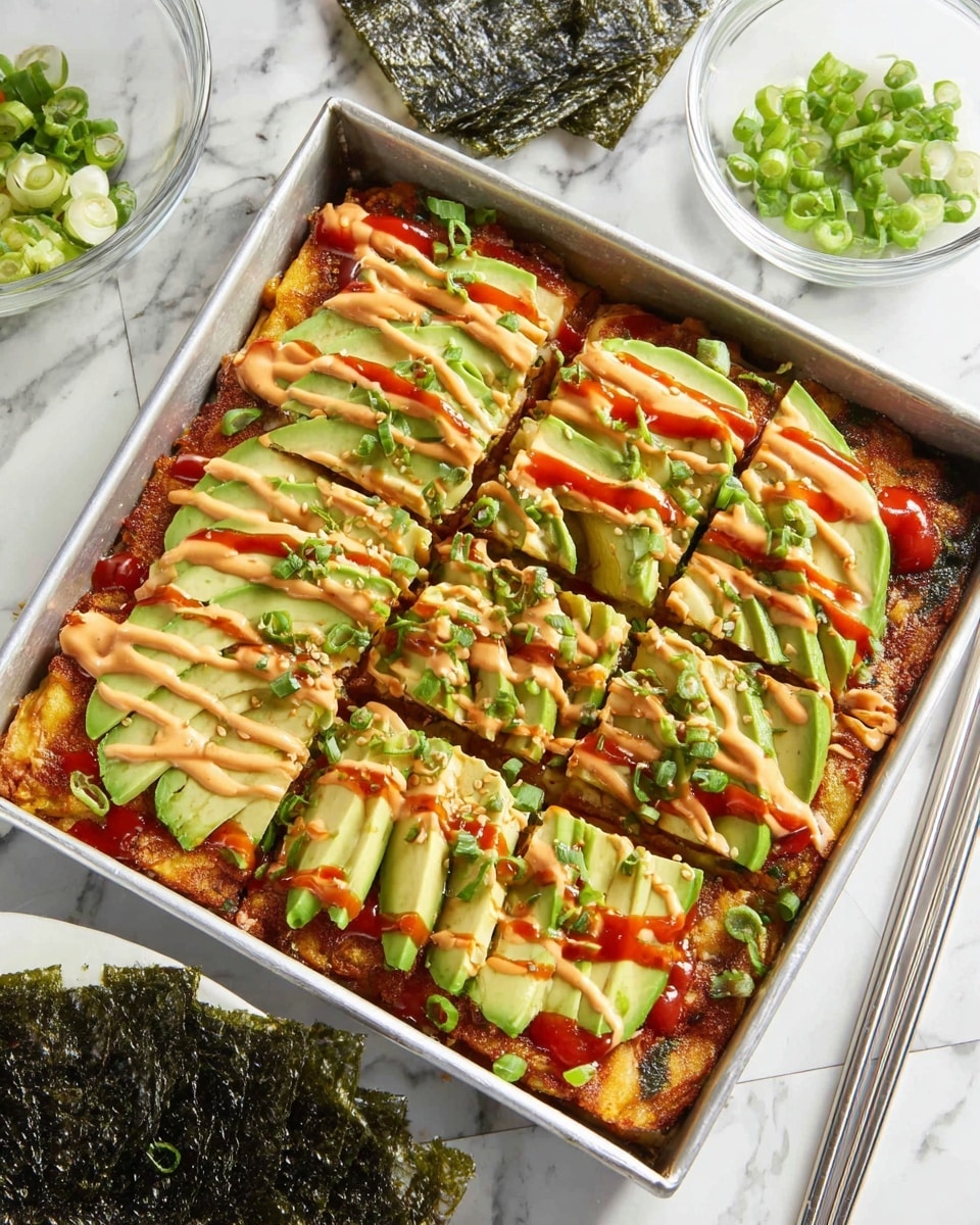 A square pan filled with a layered dish starting with a golden brown base, topped with thick slices of green avocado arranged evenly, drizzled in a crisscross pattern with a creamy light orange sauce and a bright red sauce. The dish is garnished with small pieces of chopped green onions scattered on top. To the side, there is a clear glass bowl with more chopped green onions, a stack of dark green seaweed sheets on a white marbled surface, and a pair of silver chopsticks resting next to the pan. Photo taken with an iphone --ar 4:5 --v 7