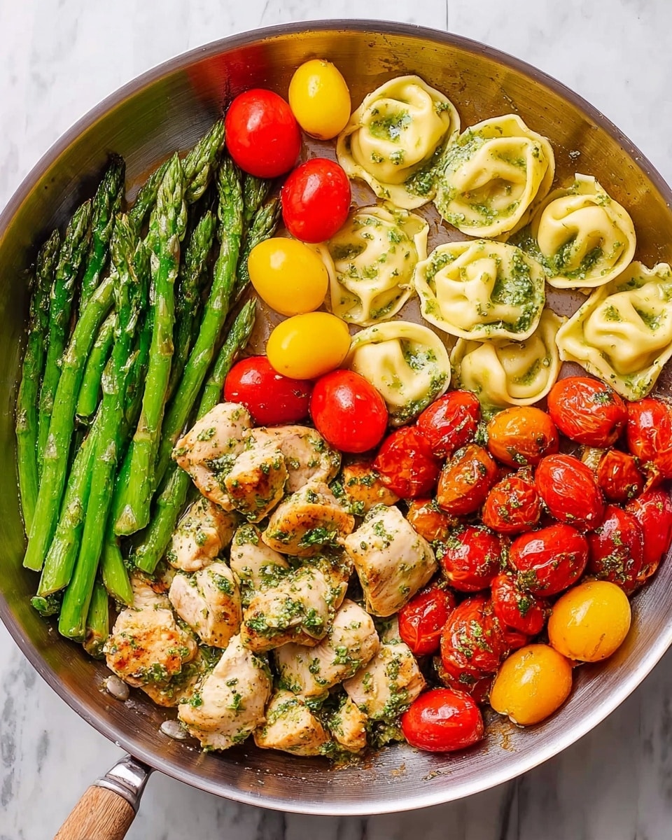 A round silver pan holds a colorful dish divided into three main sections. On the left, a layer of bright green asparagus spears lies neatly side by side with a few whole yellow and red cherry tomatoes scattered on top. To the right of the asparagus is a pile of light golden, folded tortellini pasta, coated in a light green herb sauce with some herbs visible. The bottom right section has pieces of cooked chicken mixed with halved red and yellow cherry tomatoes, all topped with the same green herb sauce. The pan is placed on a white marbled surface. photo taken with an iphone --ar 4:5 --v 7