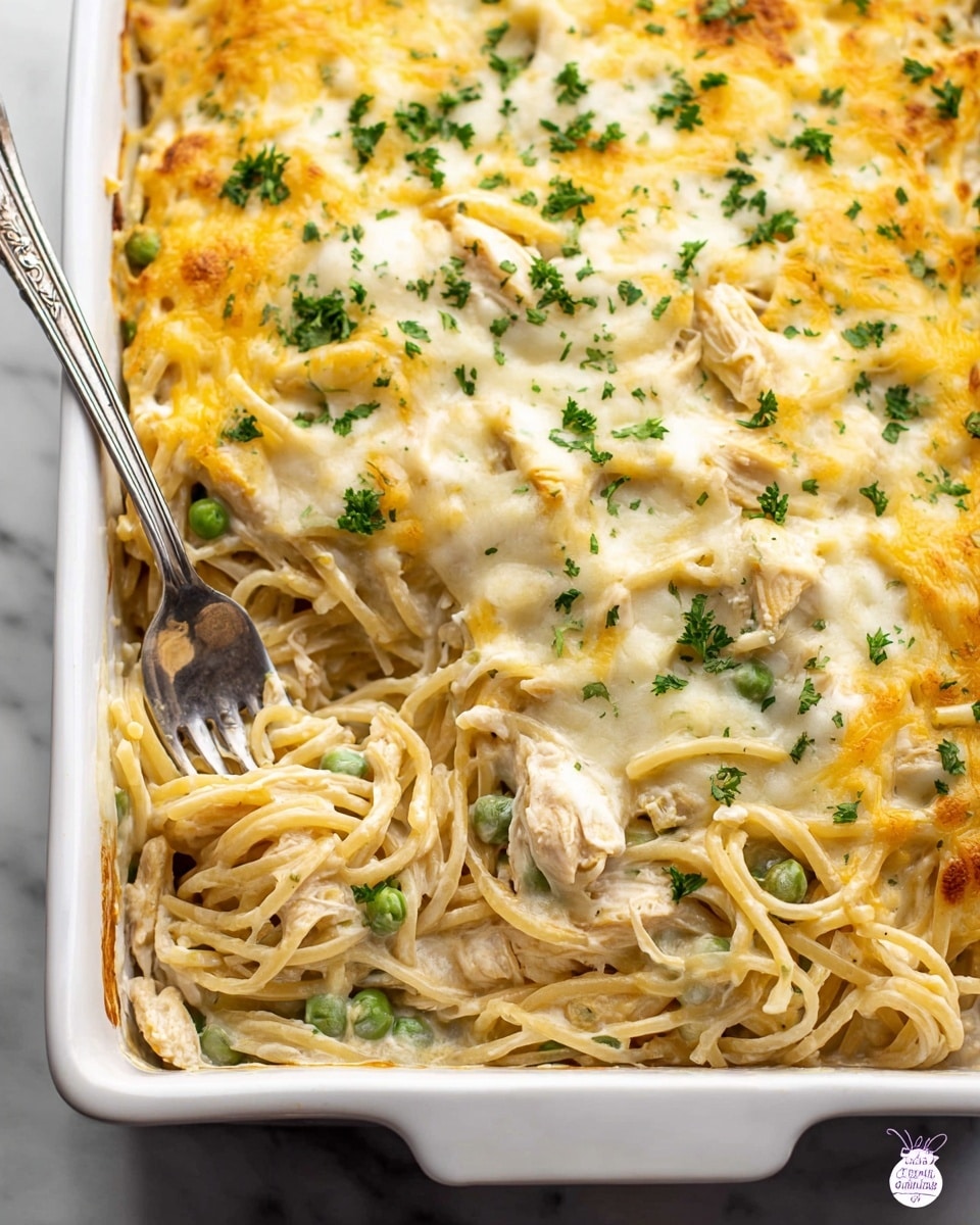 The image shows a white rectangular baking dish filled with a creamy baked pasta casserole. The dish has three main layers: the bottom layer is made of pale off-white cooked pasta mixed with green peas and pieces of chicken; the middle layer has a thick creamy white sauce; the top layer is a golden yellow melted cheese with a few melted white cheese patches, sprinkled evenly with small chopped green herbs. A silver fork and spoon are placed inside the dish, with some pasta twirled onto the fork, showing the creamy texture. The background surface is a white marbled texture. photo taken with an iphone --ar 4:5 --v 7