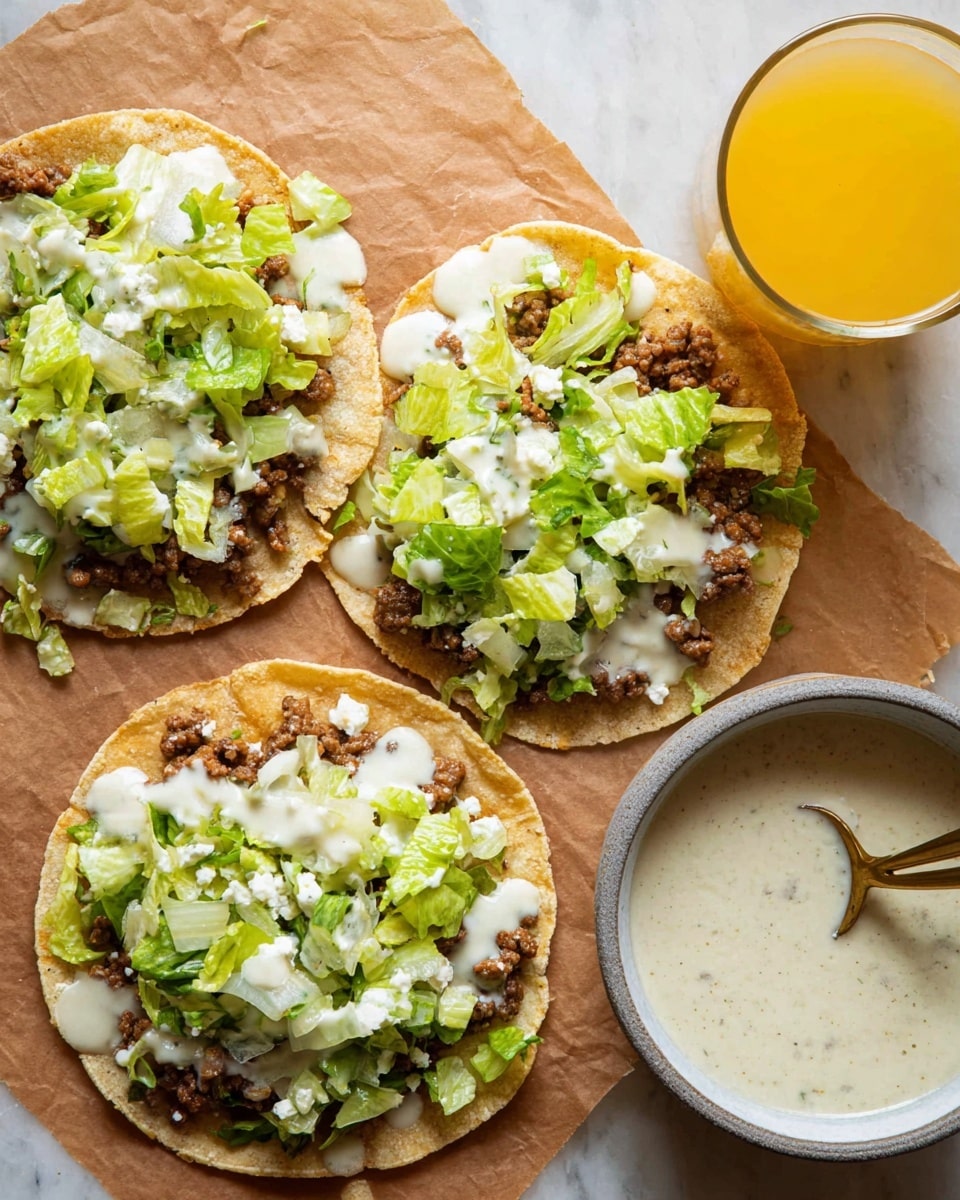 The image shows three small round corn tortillas laid flat on a brown paper on a white marbled surface. Each tortilla is topped with a cooked, flat layer of seasoned ground meat that is brown and slightly textured. Over the meat, there is a layer of light green chopped lettuce, unevenly spread, with some pieces bigger than others. A creamy white sauce is drizzled on top of the lettuce and meat in a loose, uneven pattern. To the right of the tortillas, there is a glass filled with a yellow-orange drink. In the bottom right corner, a white bowl with a grey rim contains more creamy white sauce, with a brass-colored spoon partially resting inside. Photo taken with an iphone --ar 4:5 --v 7