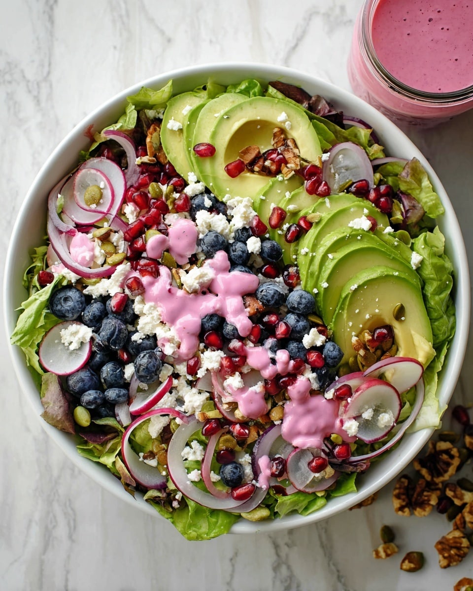 A fresh salad is arranged in a white bowl on a white marbled surface. The base is made of bright green lettuce leaves. On top, there are evenly spread slices of green avocado and thin round slices of purple and white radish. Blueberries and shiny red pomegranate seeds add pops of color. Thin slices of pale red onion are scattered among the ingredients. Crumbled white cheese is spread over the salad. A pink creamy dressing is drizzled on top. Some nuts are mixed in, adding a shiny brown texture. A glass jar filled with pink dressing is visible near the bowl. Photo taken with an iphone --ar 4:5 --v 7