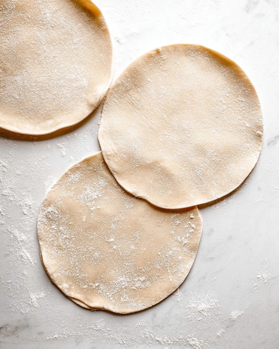 Three round dough pieces lie flat on a white marbled surface. Each dough circle is thin and light beige with a dusting of white flour scattered lightly across their tops. They have a smooth texture with soft edges that are slightly uneven. The dough pieces are spread out with some space between them, showing a simple, clean preparation stage. Photo taken with an iphone --ar 4:5 --v 7