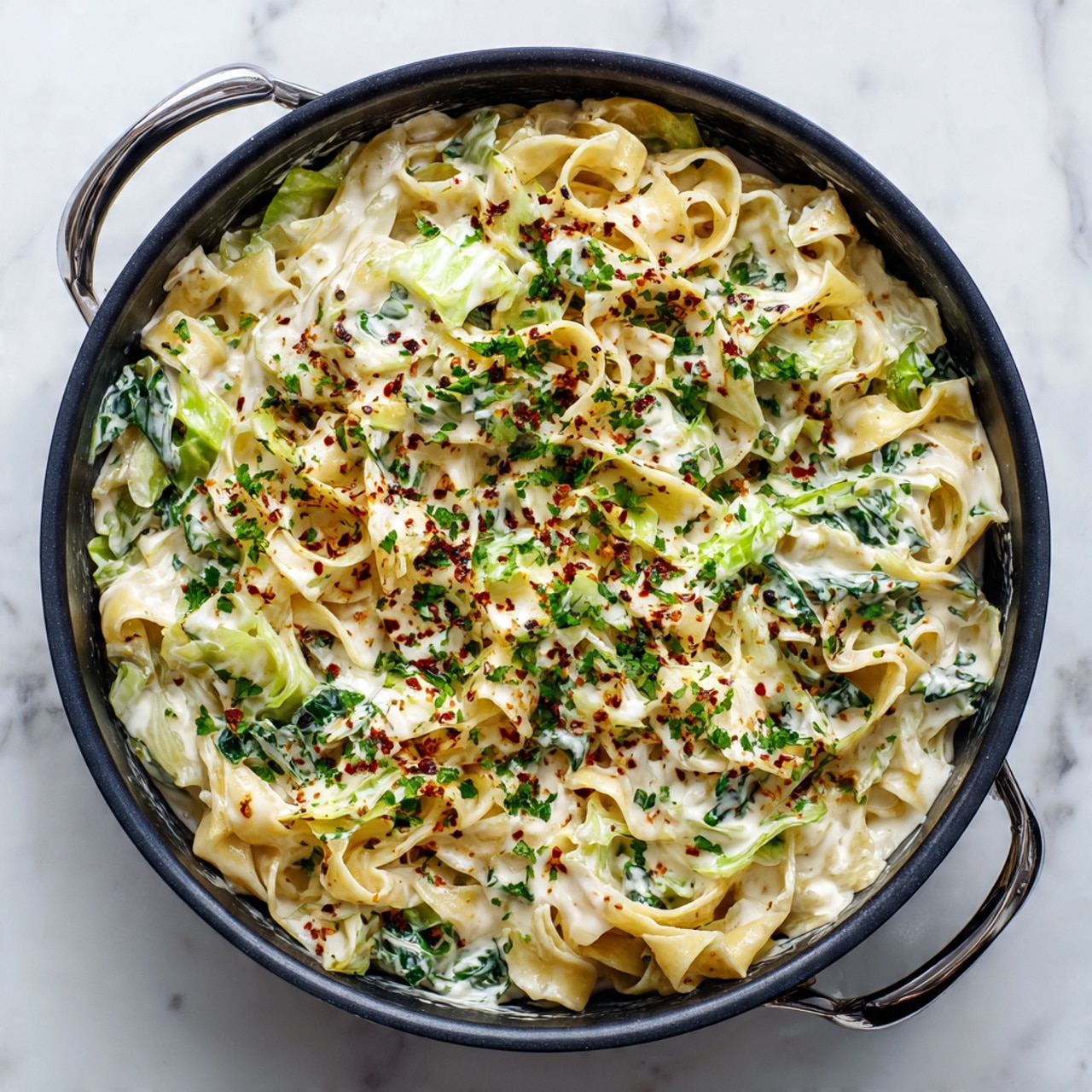 In a black pan, there is a creamy pasta dish with layers of wide, flat noodles coated in a thick, white sauce mixed with green leafy vegetables. The noodles are soft and curled, spread evenly throughout the pan. Small bits of dark green herbs and a light sprinkle of reddish spices are scattered on top, adding color and texture. The creamy sauce looks smooth and rich, surrounding the noodles and leaves. The pan is placed on a white marbled surface. Photo taken with an iphone --ar 4:5 --v 7