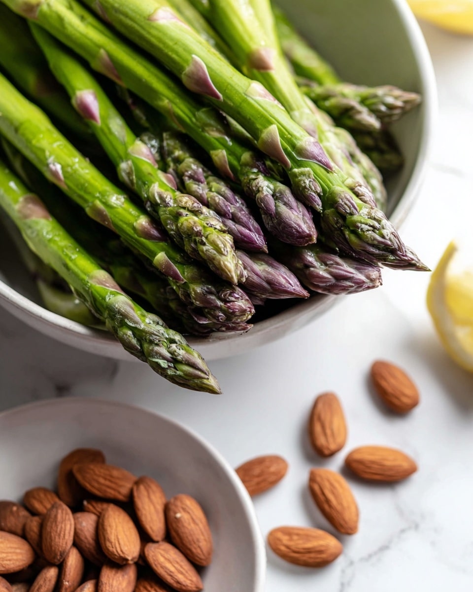 A fresh salad in a white bowl with mixed green leaves like lettuce and spinach forming the base layer, topped with bright green peas, whole almonds scattered around, thinly sliced red radishes with white centers, and small dollops of white soft cheese. There are also green asparagus spears placed on top. On the white marbled surface around the bowl, some almonds are placed, with a small white round bowl of green dressing to the left and a silver spoon beside it. A gray textured cloth with more almonds and a silver fork are on the upper right side of the image. Photo taken with an iphone --ar 4:5 --v 7