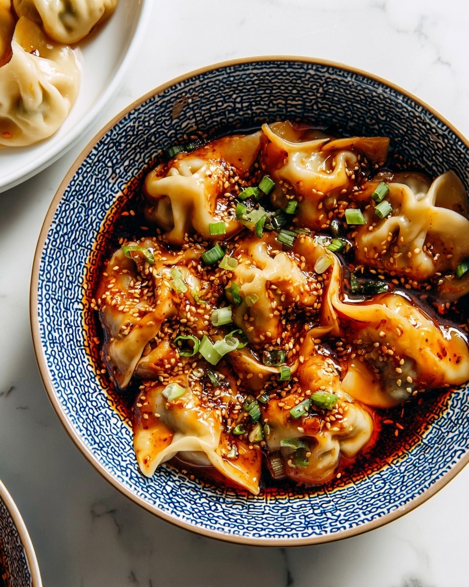 A bowl filled with many light beige dumplings covered in a shiny, dark red chili oil sauce. The dumplings have a soft texture with some folds and wrinkles on top. Sprinkled over the dumplings are small white sesame seeds and bright green chopped scallions. The bowl has a detailed blue and white woven pattern on the rim and outside. The scene is set on a white marbled surface with part of a white plate with more dumplings visible in the top left corner. photo taken with an iphone --ar 4:5 --v 7
