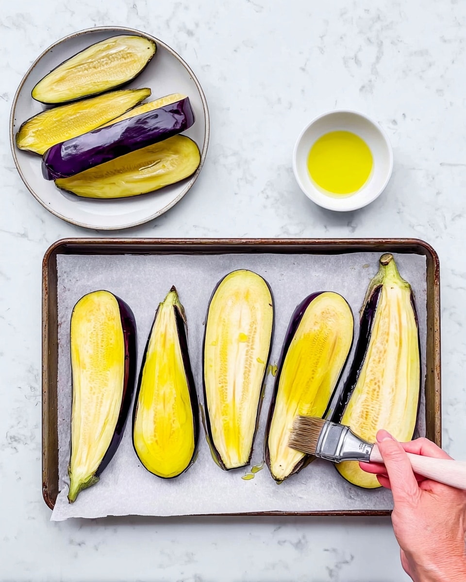 The image shows a baking tray lined with parchment paper holding seven slices of eggplant, each with a mix of dark purple skin and pale yellow inner flesh. Two halves of eggplant without skin are also on the tray. To the left, there is a white plate with more eggplant slices stacked unevenly and a small white bowl filled with yellow oil. A woman's hand is brushing oil onto one of the large eggplant slices on the right side of the tray, holding a silver brush. All items are placed on a white marbled surface. photo taken with an iphone --ar 4:5 --v 7